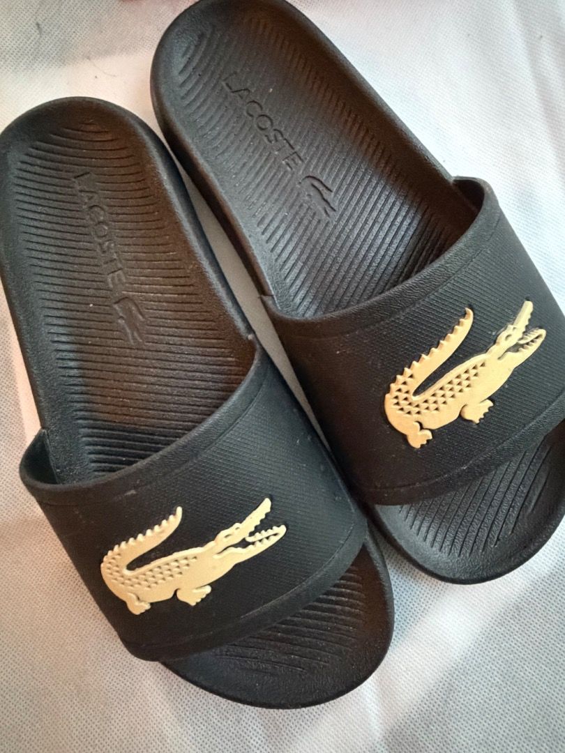 Black Lacoste Slides with Gold Crocodile Logo (Category: Slippers & Slides) located in Manila. Submitted by mypersonalclothes (Listing ID 1440734723, Image 1). Description: - Classic black Lacoste slides - Features iconic gold crocodile logo on the strap - Textured footbed with embossed Lacoste name for grip - Easy slip-on design - Ideal for casual wear or after sports.
