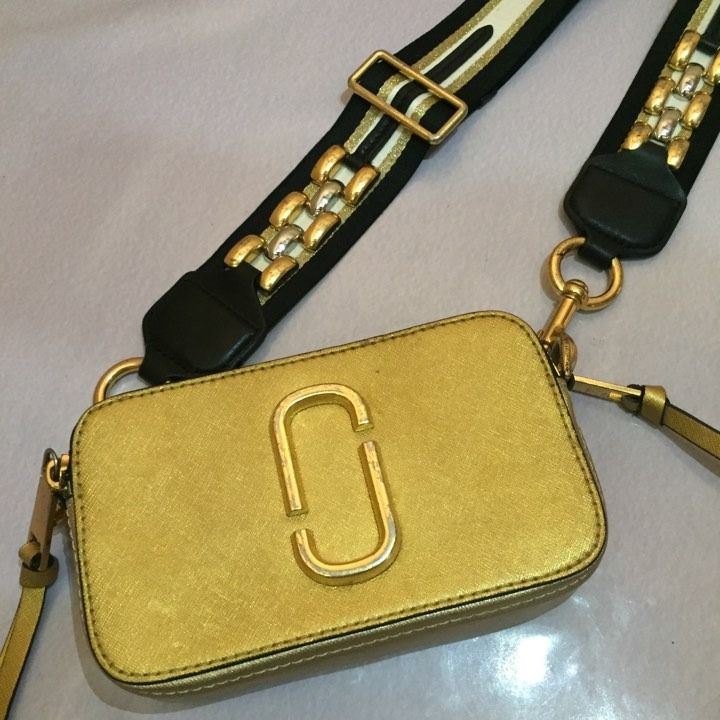 MARC JACOBS Snapshot Camera Bag METALLIC GOLD (Category: Luxury Bags & Wallets) located in Lucena. Submitted by brkrobert (Listing ID 1440582515, Image 3). Description: - Authentic Gold Marc Jacobs Snapshot camera bag - Features a detachable strap with black, white, and gold stripes - Strap is adorned with stylish metal stud details - All hardware is gold-tone - Shows some signs of wear on the hardware and strap, adding character.