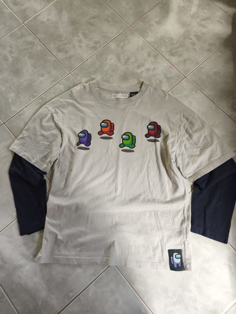 Among Us Double Layered T-shirt (Category: Tshirts & Polo Shirts ) located in San Carlos. Submitted by applemanga71941 (Listing ID 1435722270, Image 2). Description: - Double-layered t-shirt featuring Among Us characters. - Outer layer color: Beige. - Inner layer color: Navy Blue. - Front design: Multiple Among Us characters. - Back design: "IMPOSTOR" text and two additional Among Us characters. - Includes a tag on the collar..