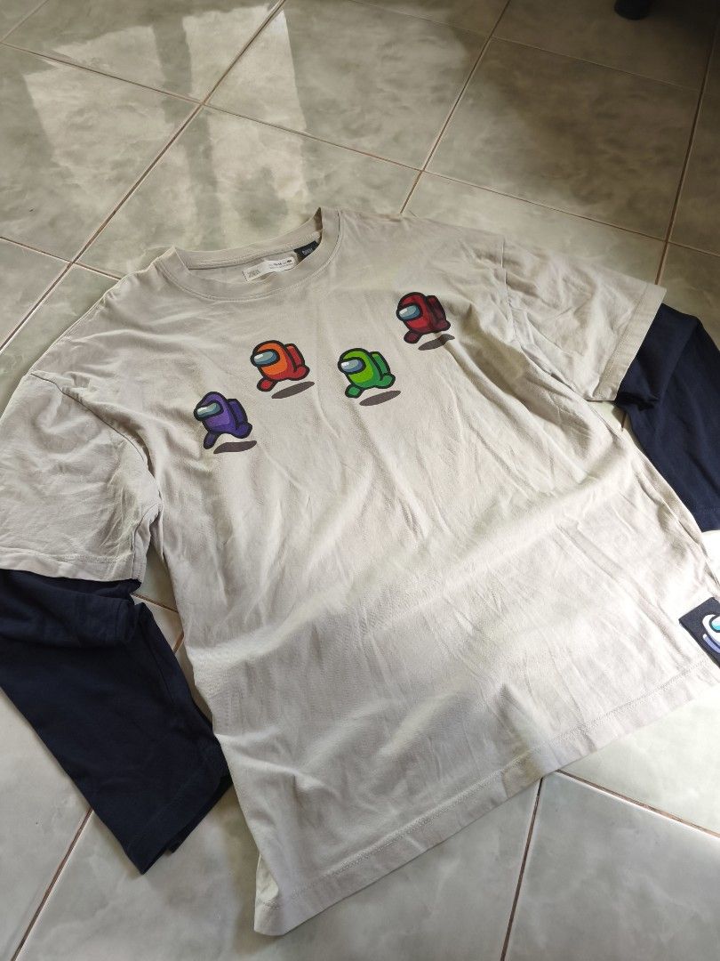 Among Us Double Layered T-shirt (Category: Tshirts & Polo Shirts ) located in San Carlos. Submitted by applemanga71941 (Listing ID 1435722270, Image 3). Description: - Double-layered t-shirt featuring Among Us characters. - Outer layer color: Beige. - Inner layer color: Navy Blue. - Front design: Multiple Among Us characters. - Back design: "IMPOSTOR" text and two additional Among Us characters. - Includes a tag on the collar..