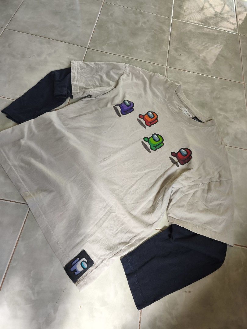 Among Us Double Layered T-shirt (Category: Tshirts & Polo Shirts ) located in San Carlos. Submitted by applemanga71941 (Listing ID 1435722270, Image 1). Description: - Double-layered t-shirt featuring Among Us characters. - Outer layer color: Beige. - Inner layer color: Navy Blue. - Front design: Multiple Among Us characters. - Back design: "IMPOSTOR" text and two additional Among Us characters. - Includes a tag on the collar..