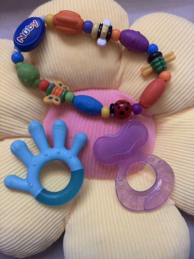 Nuby Teething Set (Category: Soothers & Pacifiers) located in Manila. Submitted by sufelme_online_shop (Listing ID 1435782634, Image 2). Description: - Nuby Teething Set: - Includes a bracelet, hand-shaped teether, and pacifier-shaped teether. - Bracelet features colorful beads with bee, ladybug, and butterfly. - Hand-shaped teether is blue with a darker blue grip. - Pacifier-shaped teether is purple. - Designed to soothe and comfort babies durin
