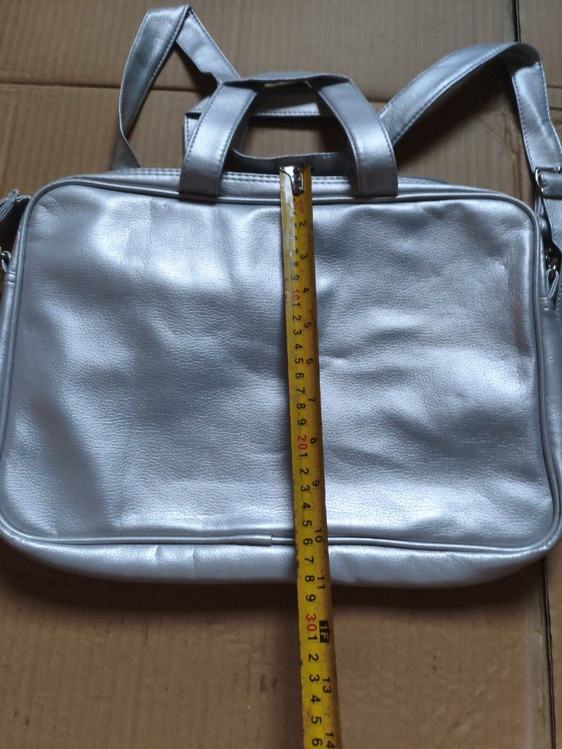 Silver Laptop Bag with Shoulder Strap (Category: Laptop Bags & Sleeves) located in Pasig City. Submitted by coolphoenix-29ac (Listing ID 1435818566, Image 3). Description: - Silver laptop bag - Includes shoulder strap and top handles - Main compartment and smaller interior pocket - Made of smooth, faux leather material - Rectangular shape - Adjustable shoulder strap.