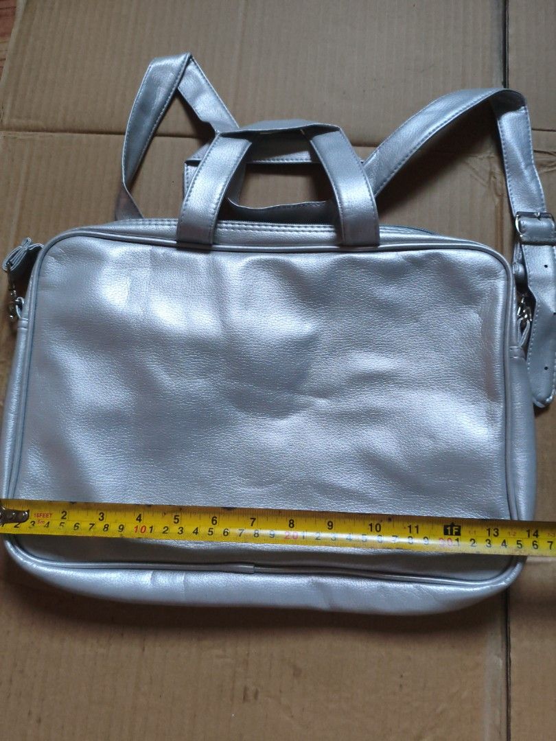 Silver Laptop Bag with Shoulder Strap (Category: Laptop Bags & Sleeves) located in Pasig City. Submitted by coolphoenix-29ac (Listing ID 1435818566, Image 2). Description: - Silver laptop bag - Includes shoulder strap and top handles - Main compartment and smaller interior pocket - Made of smooth, faux leather material - Rectangular shape - Adjustable shoulder strap.