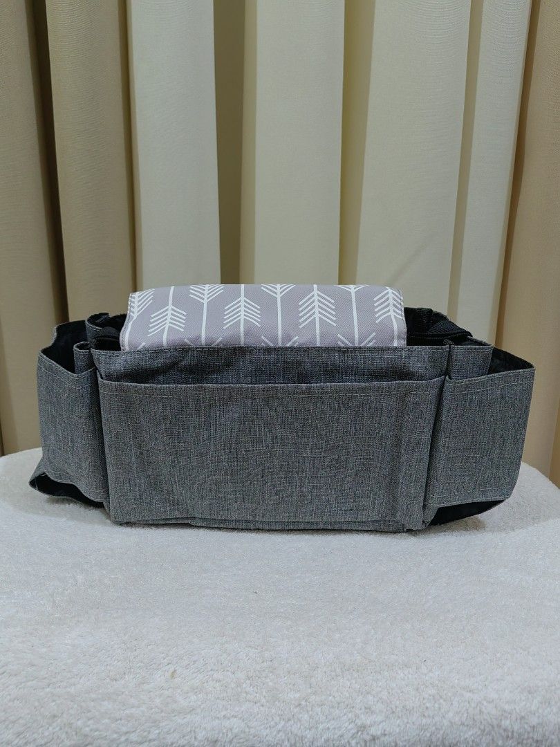 Stroller Organizer with Arrow Design (Category: Strollers) located in Makati City. Submitted by prelovedtreatedwithlove (Listing ID 1435831541, Image 2). Description: - Stroller organizer with multiple pockets for storage. - Features a stylish gray exterior. - Includes a flap with an arrow design. - Made from durable fabric. - Secure velcro closure. - Convenient carrying handle. - Interior with multiple compartments. -No issue A-101.