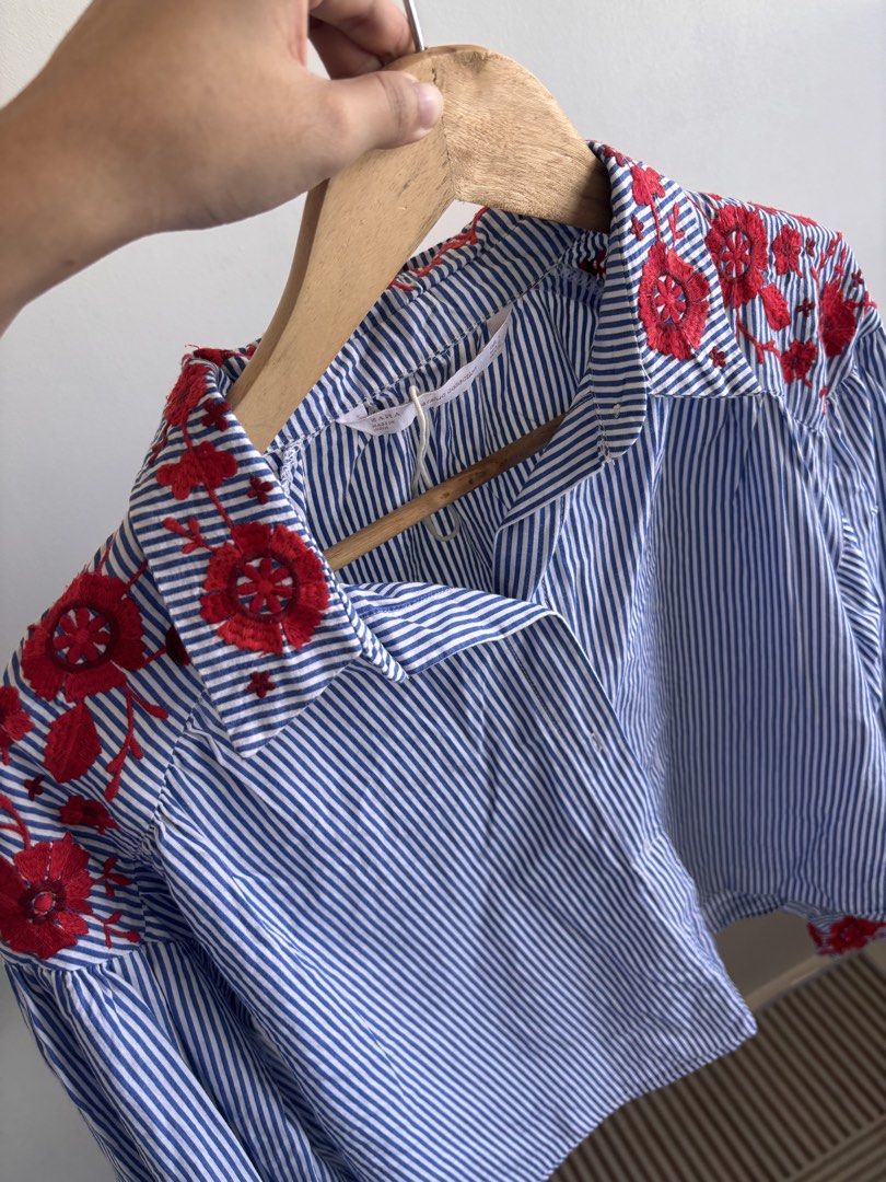 Zara Trafaluc Embroidered Striped Blouse (Category: Blouses) located in Manila. Submitted by taguigcloset (Listing ID 1435769178, Image 1). Description: - Zara Trafaluc blouse - Blue and white stripes - Red floral embroidery - Collared neckline - Long sleeves - Size S Rfs: decluttering honest issue: small tear on the sleeve - see photo.