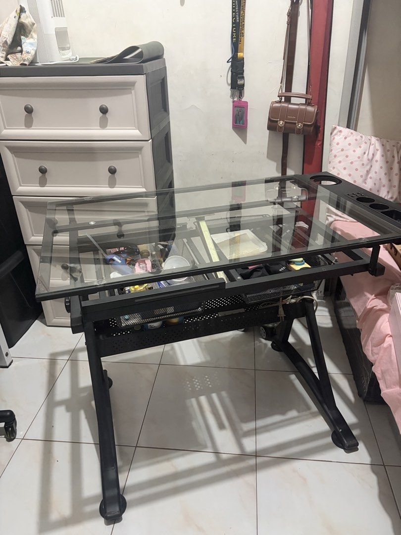 Glass Top Drafting Table with Storage Drawers (Category: Tables & Sets) located in Manila. Submitted by orissa.lenisse._663 (Listing ID 1440902832, Image 3). Description: - Adjustable glass top drafting table - Sturdy black metal frame - Two convenient mesh storage drawers underneath - Side organizer with cup holders and pen slots - Ideal for art, drawing, and crafting projects - Equipped with wheels for easy mobility.