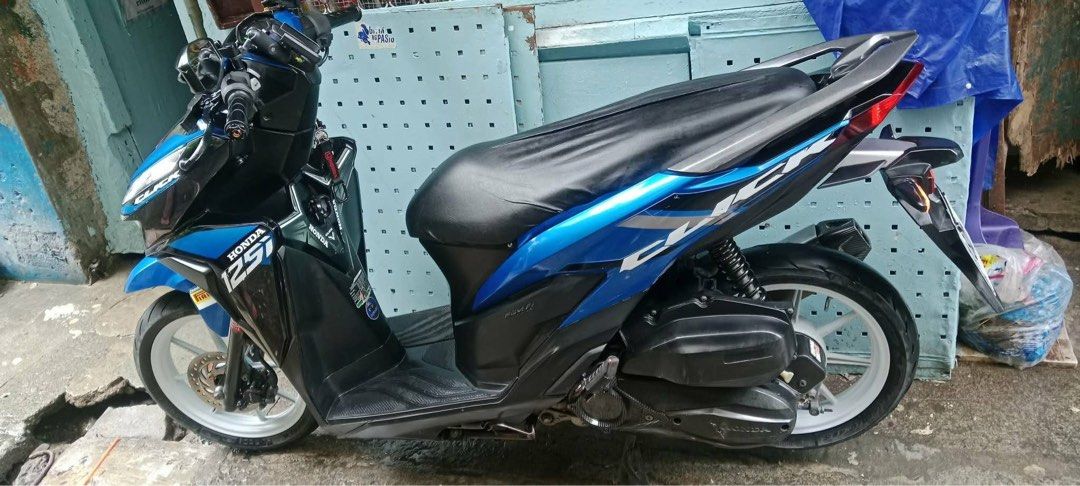Honda Click 125i Motorcycle Blue (Category: Motorbikes for Sale) located in Quezon City. Submitted by jammatriano (Listing ID 1440863866, Image 2). Description: Honda Click 125i scooter in a vibrant blue. Has a sleek design with sharp headlights. The seat is covered with a black seat cover. White rims add a nice contrast. Ready for the road. Great for city commuting..