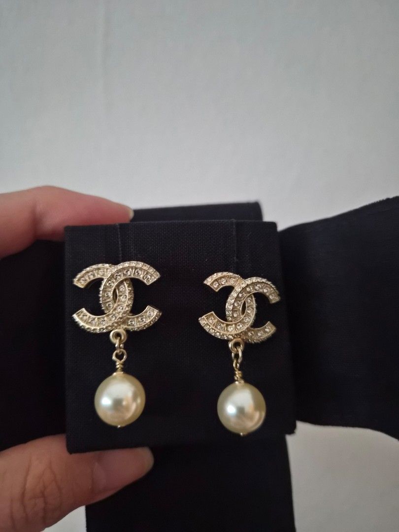 Chanel CC Pearl Drop Earrings Gold (Category: Earrings) located in Singapore. Submitted by nicki3 (Listing ID 1440964332, Image 1). Description: - Classic Chanel earrings - Iconic CC logo with pearl drop - Gold tone finish - Accented with small crystals on the CC - Comes with original box - Perfect for elevating any outfit.