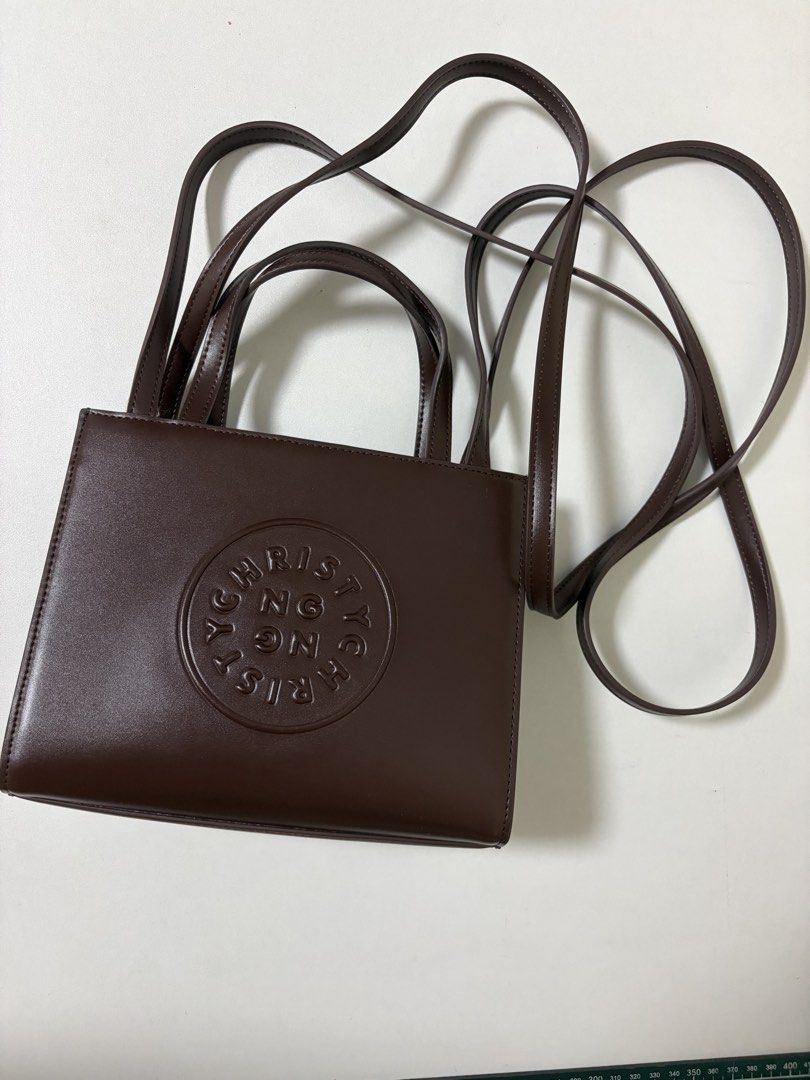 Christy Ng Brown Handbag with Shoulder Strap (Category: Shoulder Bags) located in Manila. Submitted by na.serr (Listing ID 1436031370, Image 1). Description: - Brown handbag - Top handle and shoulder strap - Rectangular shape - Circular embossed logo - Magnetic closure - Smooth, leather-like material - Perfect for everyday wear.