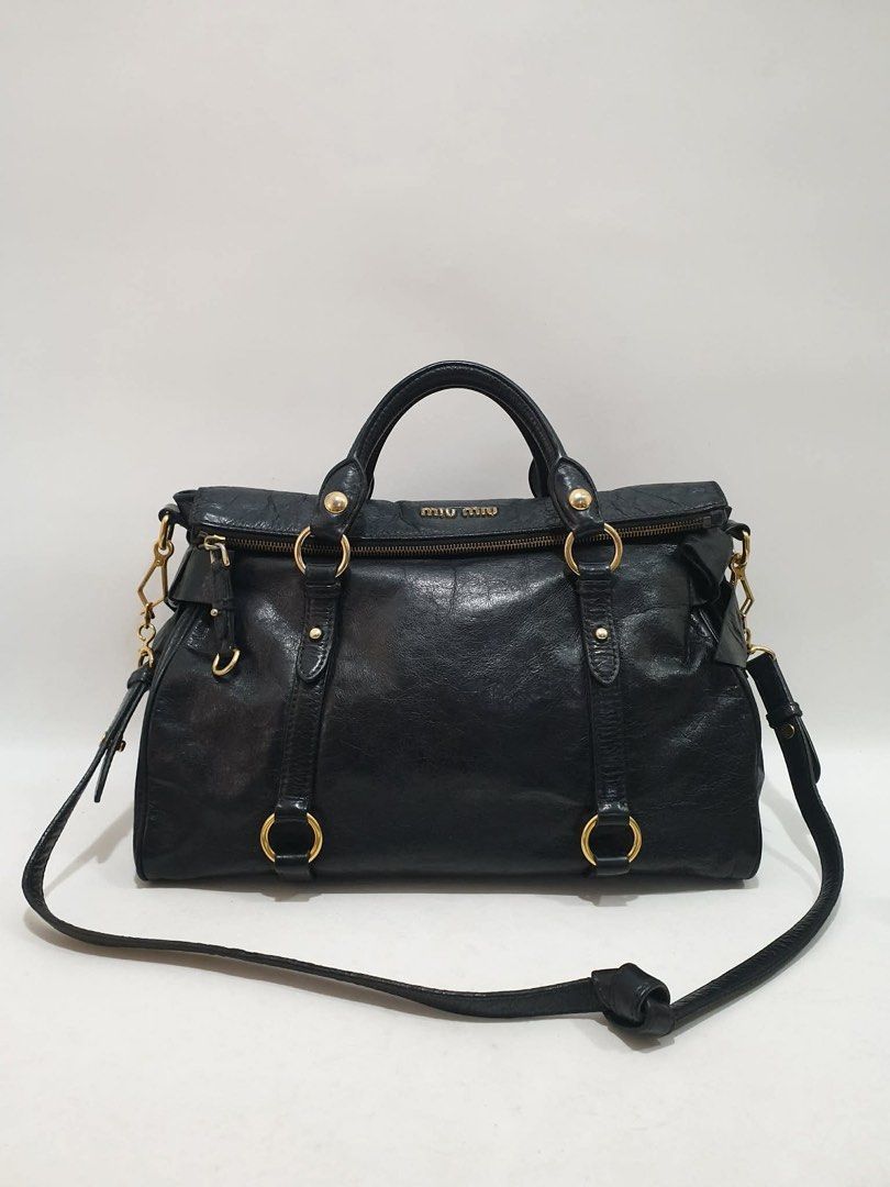 Miu Miu Vitello Lux Leather Bow Bag (Category: Luxury Bags & Wallets) located in Manila. Submitted by na.serr (Listing ID 1435970323, Image 1). Description: - Miu Miu black leather handbag - Top handle and detachable shoulder strap - Gold-tone hardware - Zip closure - Textured leather finish - Brand name visible on front.