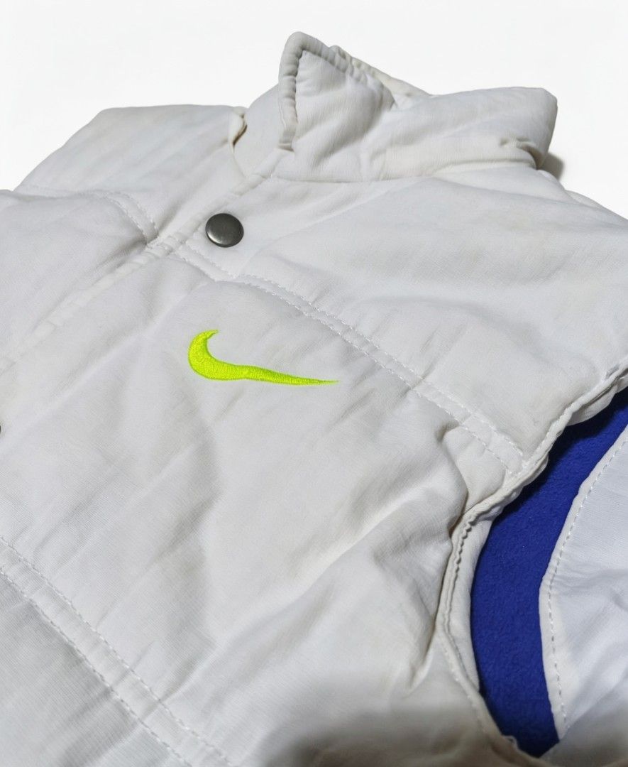 Nike Puffer Vest (Category: Vests) located in Bulacan. Submitted by rb_smn (Listing ID 1436051233, Image 2). Description: - White Nike puffer vest - Neon green Nike logo - High collar - Button and zipper closure - Two front pockets - Blue interior lining - Nike tag with product info - 100% cotton.
