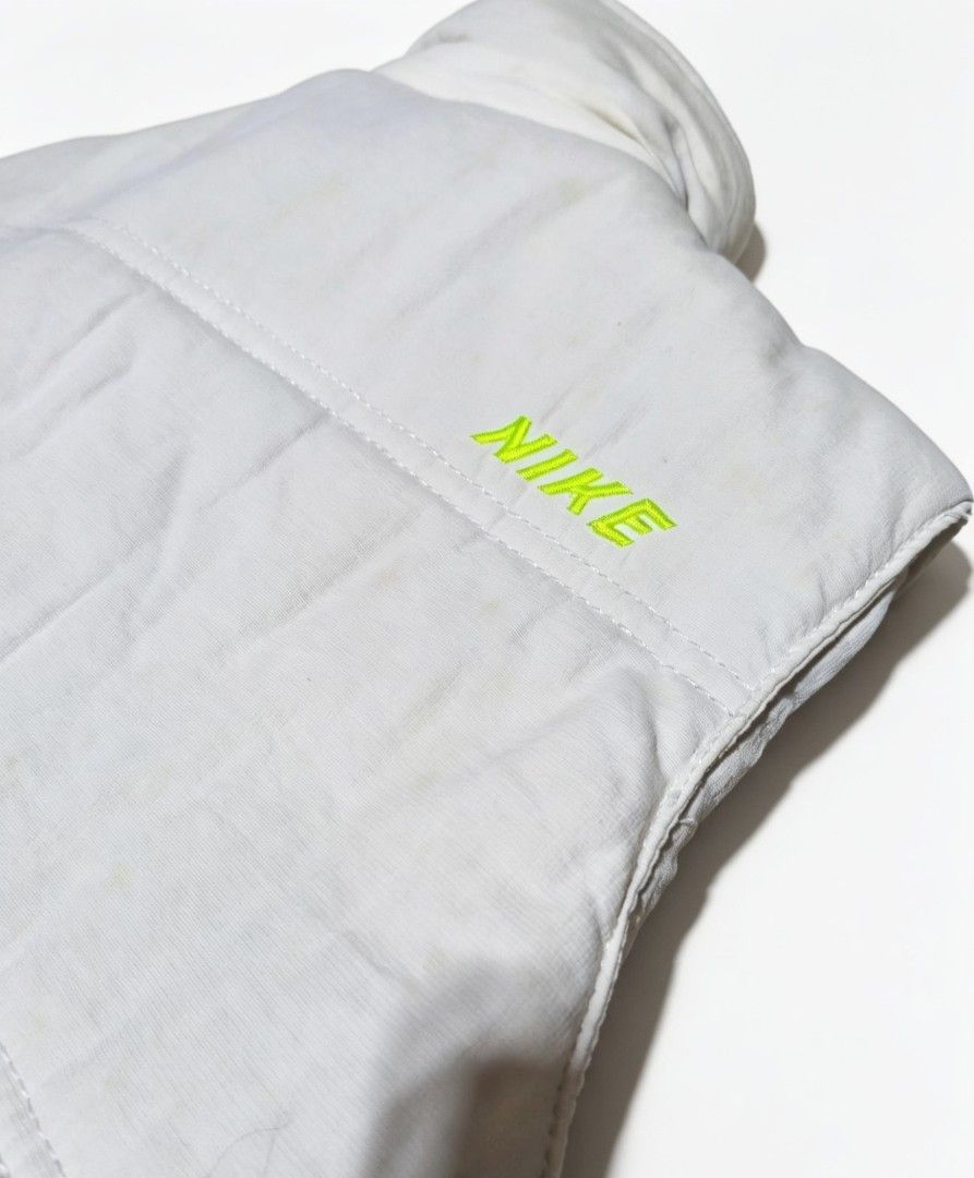 Nike Puffer Vest (Category: Vests) located in Bulacan. Submitted by rb_smn (Listing ID 1436051233, Image 3). Description: - White Nike puffer vest - Neon green Nike logo - High collar - Button and zipper closure - Two front pockets - Blue interior lining - Nike tag with product info - 100% cotton.