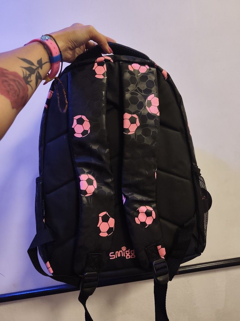 Smiggle Soccer Ball Backpack (Category: Babies & Kids Fashion) located in Manila. Submitted by margamarti35560 (Listing ID 1436086751, Image 3). Description: - Smiggle backpack with a soccer ball design. - Features a large pink and black soccer ball detail on the front. - Black backpack with pink soccer ball patterns. - Includes a handle and adjustable straps. - Has a side pocket. - Comes with a tag attached. BRANDNEW.