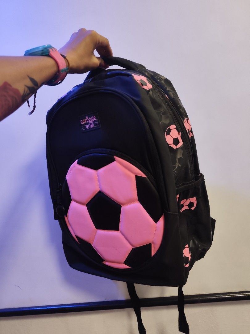 Smiggle Soccer Ball Backpack (Category: Babies & Kids Fashion) located in Manila. Submitted by margamarti35560 (Listing ID 1436086751, Image 2). Description: - Smiggle backpack with a soccer ball design. - Features a large pink and black soccer ball detail on the front. - Black backpack with pink soccer ball patterns. - Includes a handle and adjustable straps. - Has a side pocket. - Comes with a tag attached. BRANDNEW.
