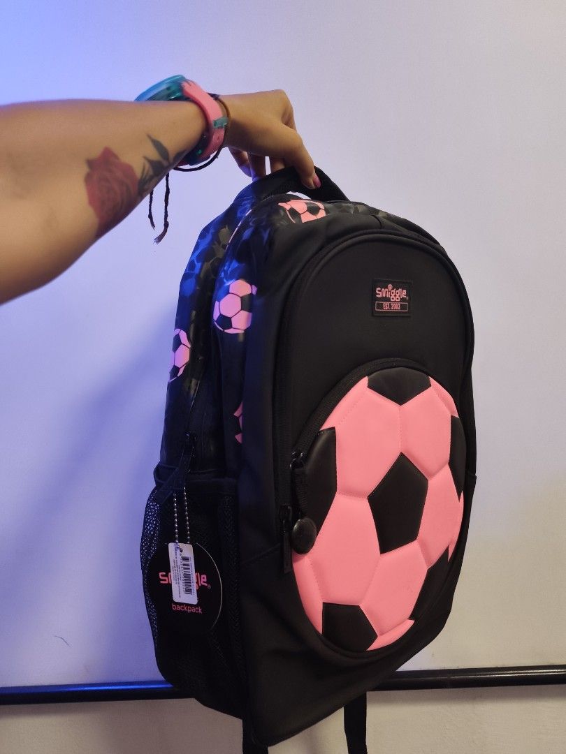 Smiggle Soccer Ball Backpack (Category: Babies & Kids Fashion) located in Manila. Submitted by margamarti35560 (Listing ID 1436086751, Image 1). Description: - Smiggle backpack with a soccer ball design. - Features a large pink and black soccer ball detail on the front. - Black backpack with pink soccer ball patterns. - Includes a handle and adjustable straps. - Has a side pocket. - Comes with a tag attached. BRANDNEW.