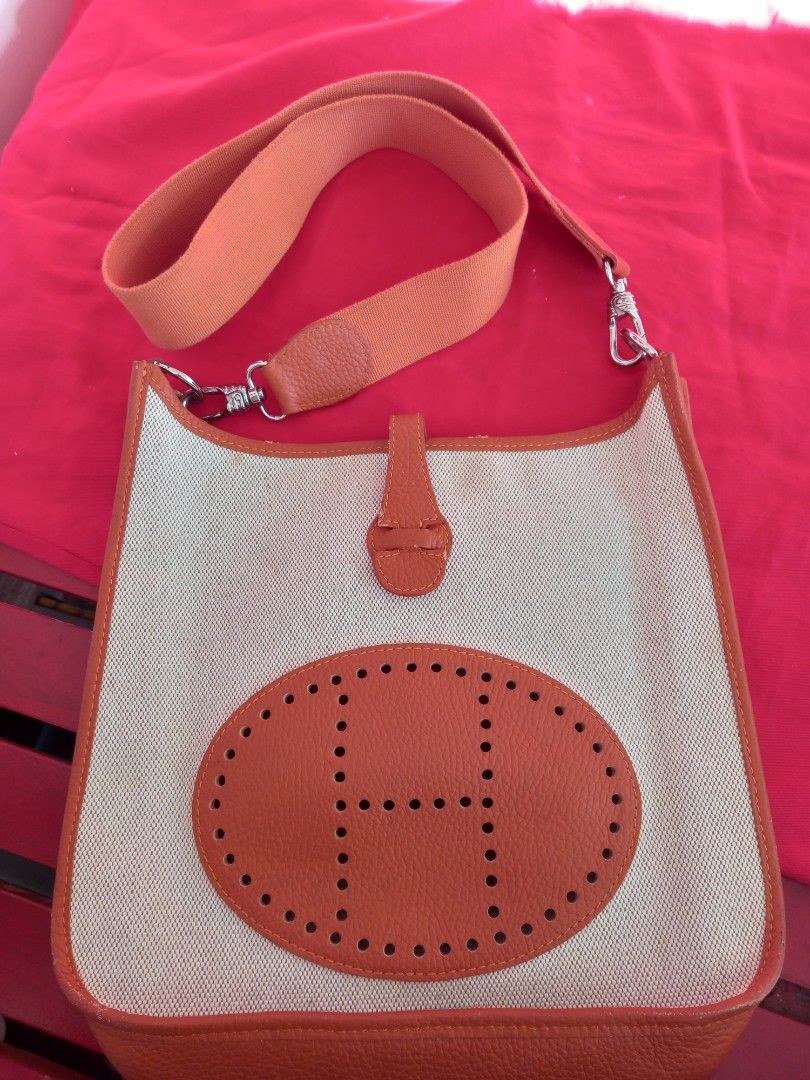 Hermes Canvas Shoulder Bag (Category: Luxury Bags & Wallets) located in Tuguegarao City. Submitted by zenphoenix-7ad615 (Listing ID 1436285959, Image 3). Description: - Orange and cream canvas shoulder bag - Orange leather trim and shoulder strap - Features an oval leather patch with the Hermes logo - Silver-tone hardware - Flap closure with leather tab 11.20 by 10.5 inches.
