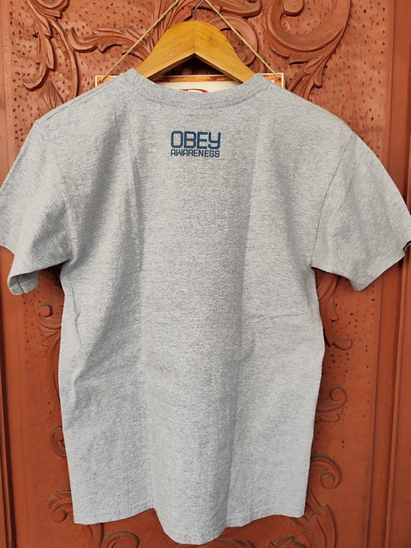 Obey We The People Graphic Tee (Category: Tshirts & Polo Shirts ) located in Pasig City. Submitted by keilahsmom (Listing ID 1436236363, Image 3). Description: Dimes: L26 W17 1/2 Size on tag: S Color rate: 10/10 Condition: Excellent 10/10 Issue(s): none Buong buo ang print walang crack or any hair line. Grey Obey t-shirt features a graphic print on the front with the words "We The People" and a portrait of a woman with a rose. The back of the shi