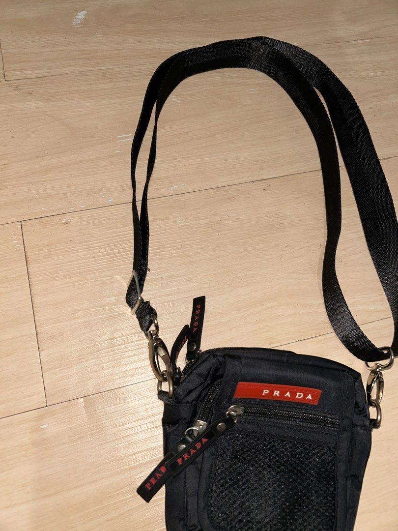 Prada Black Crossbody Bag (Category: Luxury Bags & Wallets) located in Dipolog. Submitted by adrian281994 (Listing ID 1436217566, Image 2). Description: - Prada crossbody bag - Classic black color - Iconic red Prada logo - Main compartment for essentials - Convenient front mesh pocket - Detachable and adjustable shoulder strap - Secure zipper closure - Features a small Prada zipper tag - Lined interior.