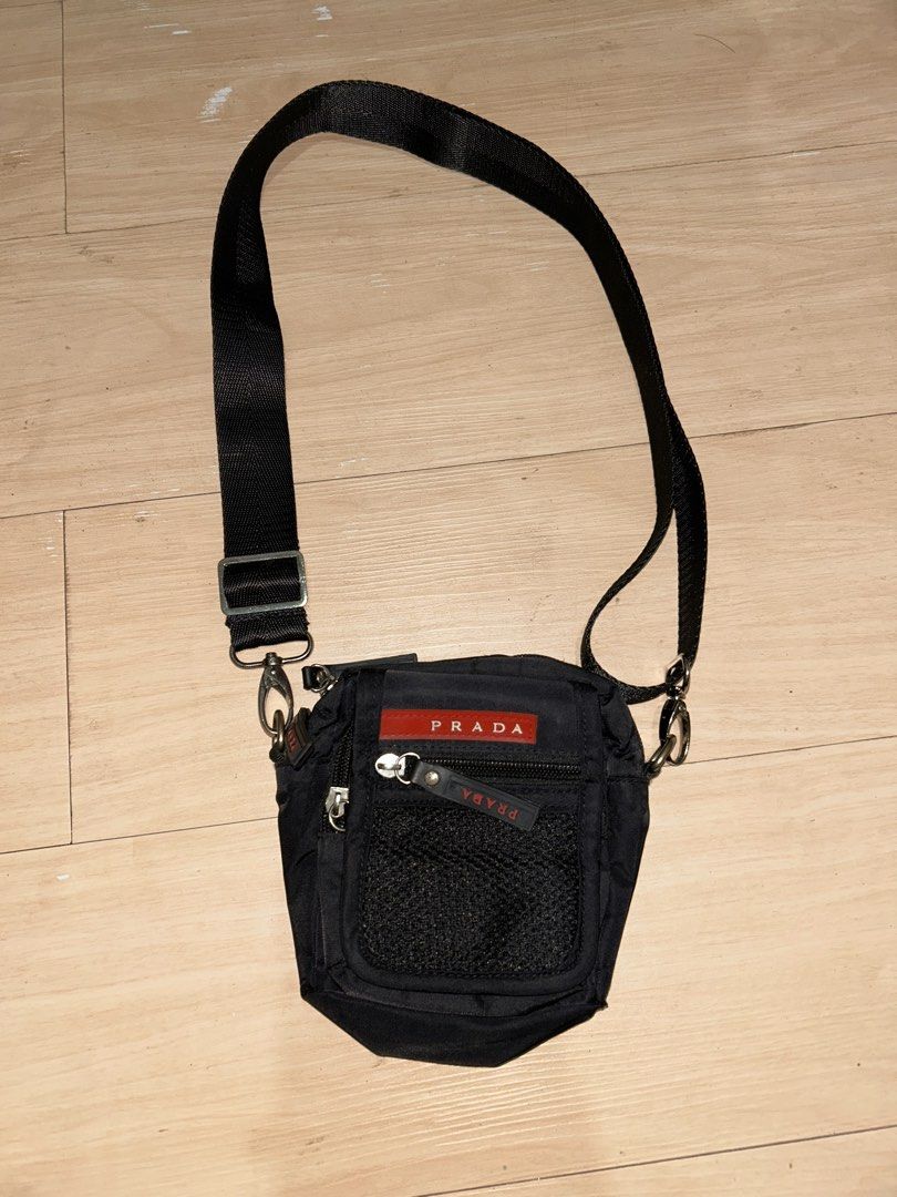 Prada Black Crossbody Bag (Category: Luxury Bags & Wallets) located in Dipolog. Submitted by adrian281994 (Listing ID 1436217566, Image 3). Description: - Prada crossbody bag - Classic black color - Iconic red Prada logo - Main compartment for essentials - Convenient front mesh pocket - Detachable and adjustable shoulder strap - Secure zipper closure - Features a small Prada zipper tag - Lined interior.