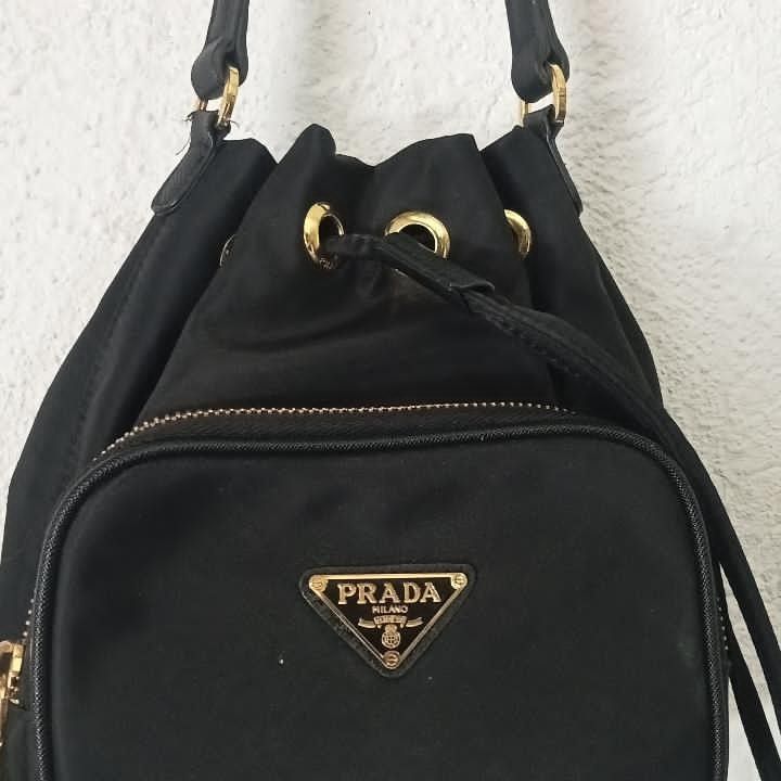 Prada Drawstring Bucket Bag (Category: Luxury Bags & Wallets) located in Manila. Submitted by kuyanyo (Listing ID 1436205786, Image 3). Description: - Authentic Prada bucket bag - Black nylon material - Gold-tone hardware - Front zippered pocket with Prada logo - Drawstring closure - Top handle - Prada logo on zipper DM IF INTIRESTED EXCELLENT CONDITION NEEDWASH.
