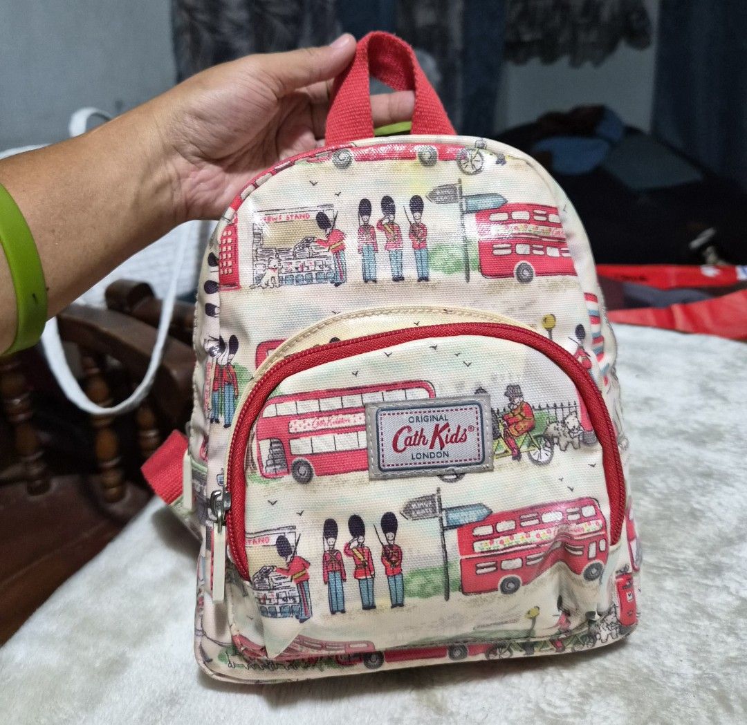 Cath Kidston Kids Mini Backpack London Streets (Category: Babies & Kids Fashion) located in Mandaue City. Submitted by chuchi152615 (Listing ID 1436469715, Image 1). Description: - Cath Kidston mini backpack - London Streets design - Red handle and straps - Front pocket - Main compartment - Zipper closure - Features illustrations of red double-decker buses, guards, and other London-themed elements - Includes Cath Kidston label.
