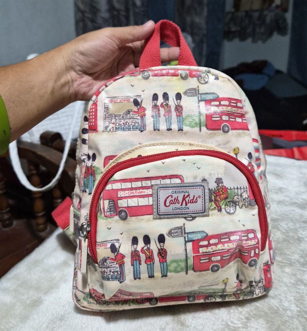 Cath Kidston Kids Mini Backpack London Streets (Category: Babies & Kids Fashion) located in Mandaue City. Submitted by chuchi152615 (Listing ID 1436469715, Image 2). Description: - Cath Kidston mini backpack - London Streets design - Red handle and straps - Front pocket - Main compartment - Zipper closure - Features illustrations of red double-decker buses, guards, and other London-themed elements - Includes Cath Kidston label.