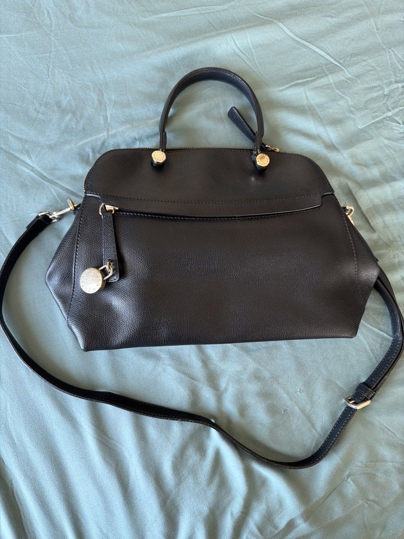 Furla Black Leather Handbag (Category: Luxury Bags & Wallets) located in Manila. Submitted by 17thfinds (Listing ID 1436352015, Image 1). Description: - Black leather handbag - Top handles and detachable shoulder strap - Zip closure - Decorative lock detail - Single compartment interior - Gold-toned hardware - Structured shape.