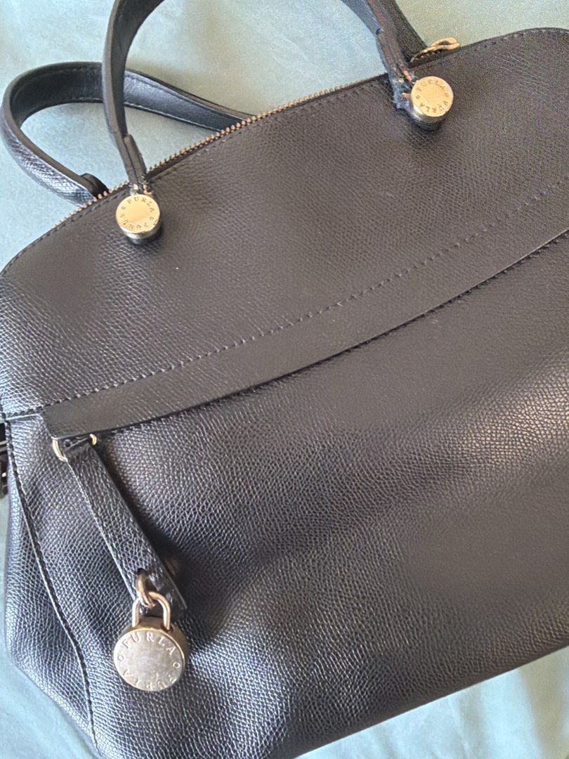 Furla Black Leather Handbag (Category: Luxury Bags & Wallets) located in Manila. Submitted by 17thfinds (Listing ID 1436352015, Image 3). Description: - Black leather handbag - Top handles and detachable shoulder strap - Zip closure - Decorative lock detail - Single compartment interior - Gold-toned hardware - Structured shape.
