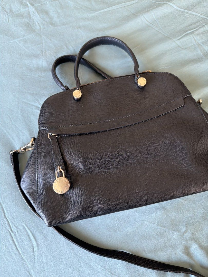 Furla Black Leather Handbag (Category: Luxury Bags & Wallets) located in Manila. Submitted by 17thfinds (Listing ID 1436352015, Image 2). Description: - Black leather handbag - Top handles and detachable shoulder strap - Zip closure - Decorative lock detail - Single compartment interior - Gold-toned hardware - Structured shape.