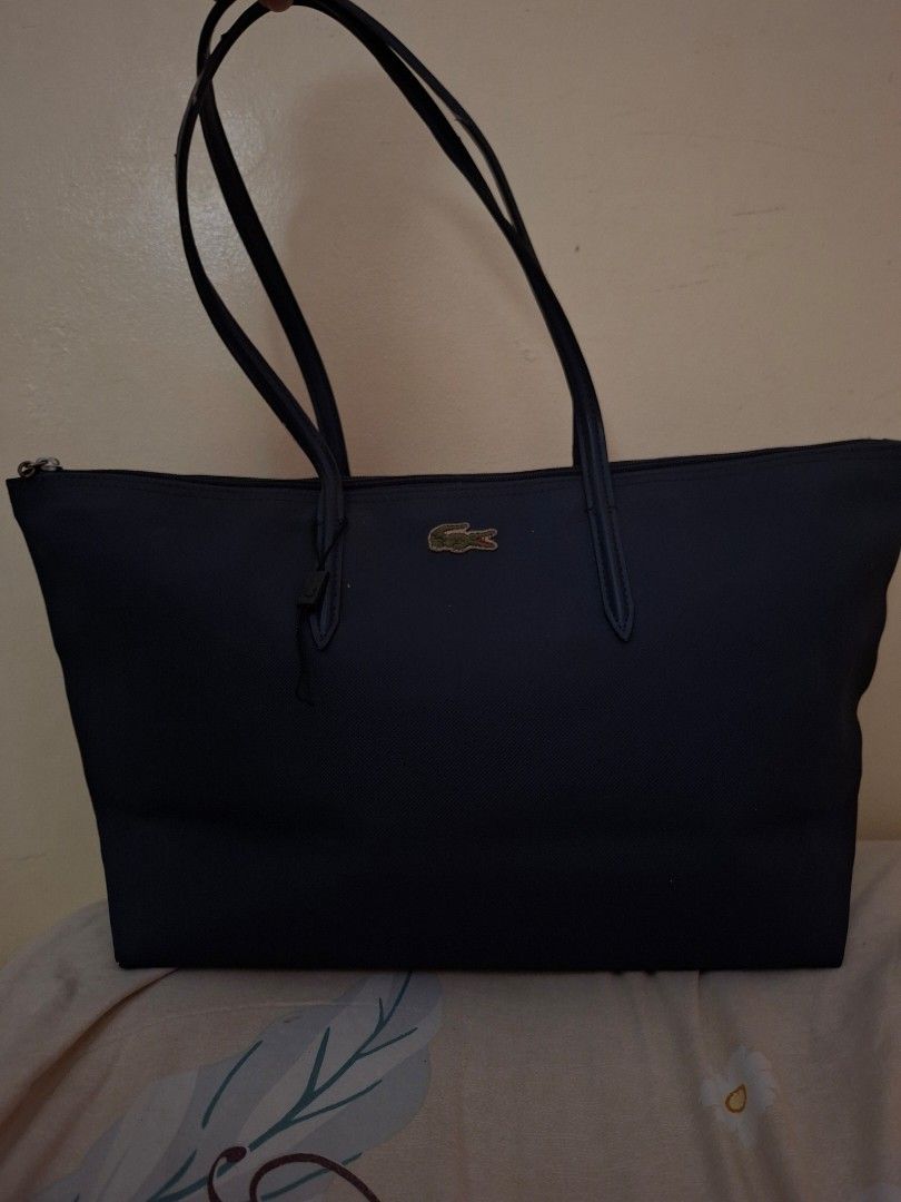 Lacoste Navy Tote Bag (Shoulder bag) (Category: Tote Bags) located in San Fernando. Submitted by lairian97 (Listing ID 1436344394, Image 2). Description: !!!GCASH PAYMENT ONLY!!! SHIPPING FEE IS COVERED BY BUYER - Lacoste navy tote bag - Gold-colored crocodile logo - Zipper closure - Two handles - Textured material - Decorative straps on the back.