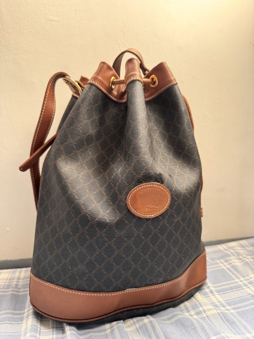 Longchamp Vintage Leather Bucket Bag (Category: Luxury Bags & Wallets) located in Rosales. Submitted by thriftingismygame (Listing ID 1436465424, Image 2). Description: - Vintage Longchamp bucket bag - Brown leather trim and strap - Drawstring closure - Crossbody strap - Brown patterned exterior - Leather logo patch - Gold-tone hardware.