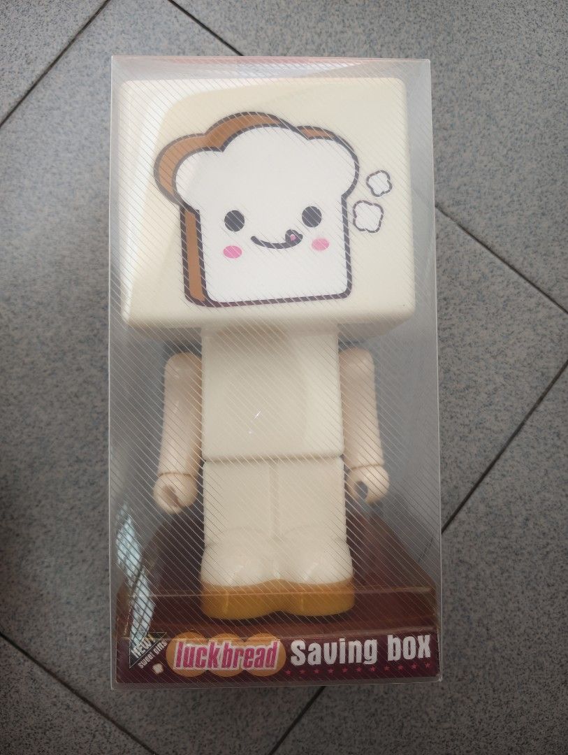 Luck Bread Saving Box (Category: Designer & Blind Box Toys) located in Pantai Remis. Submitted by winkmei (Listing ID 1436340494, Image 1). Description: Luck Bread Saving Box. It features a cute bread-shaped head and a body with arms and legs. The box is in its original packaging. The base of the box has the words "LESS IS MORE" and "It's so delicious!". This is totally new since bought ya.