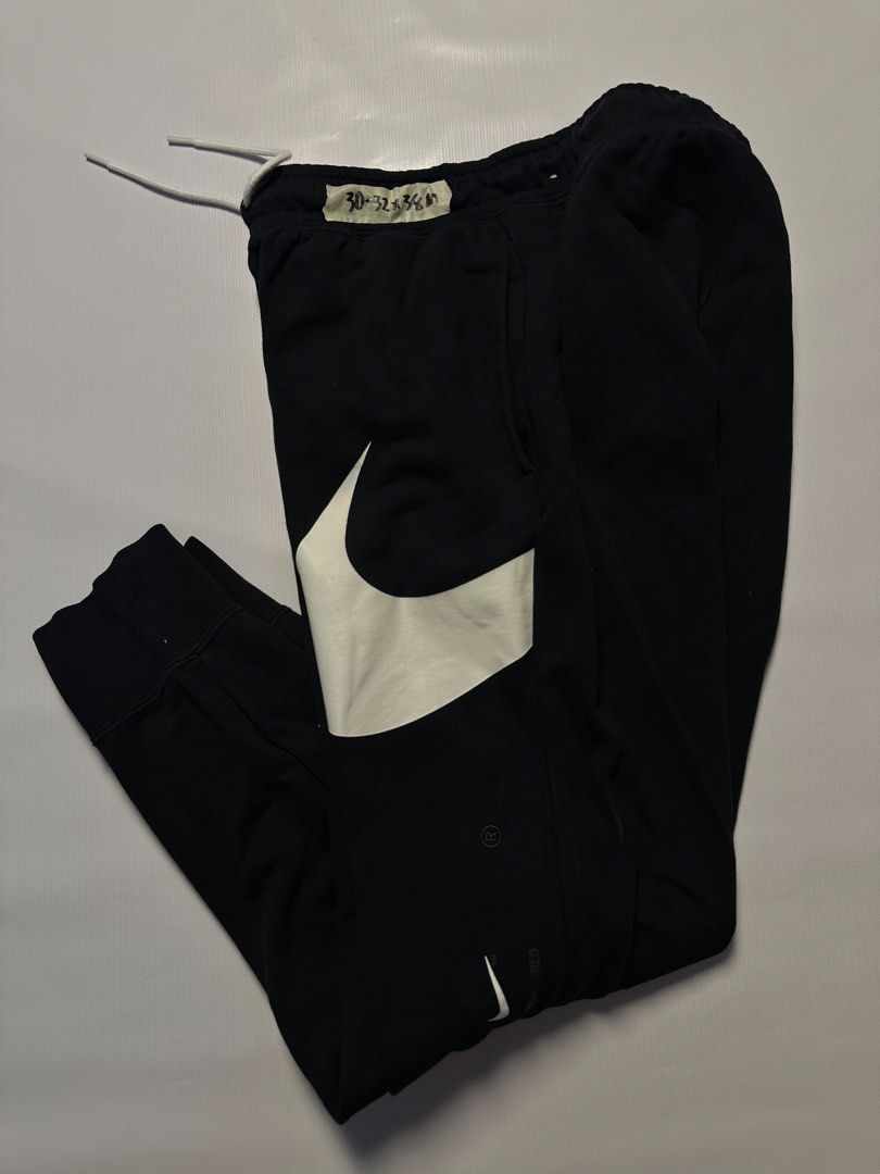 Nike Swoosh Sweatpants - Black - Size M (Category: Joggers) located in Manila. Submitted by johnedel_james (Listing ID 1436429791, Image 3). Description: Black Nike sweatpants with large white swoosh logos. Features a drawstring waist and elastic cuffs. The size is M. Made in China. The tag indicates the style code DD6092-010. The material composition is 80% cotton and 20% polyester. The waist size is indicated as 30-32.5 inches..