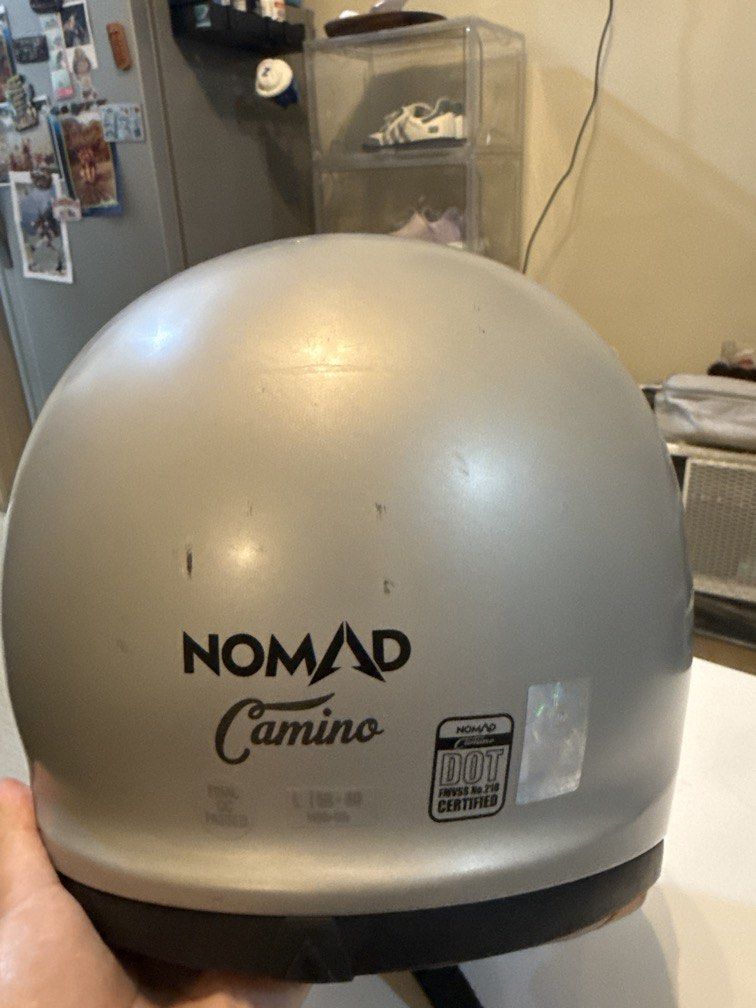 Nomad Camino Motorcycle Helmet (Category: Helmets and other Riding Gears) located in Cainta. Submitted by angelesasdfghjkl13 (Listing ID 1436422884, Image 1). Description: - Nomad Camino motorcycle helmet - Size: L (59-60) - Color: Silver exterior with black visor - DOT certified - Interior padding visible - Features "Adventure Awaits" print on the front “Kaka-ceramiclang” .