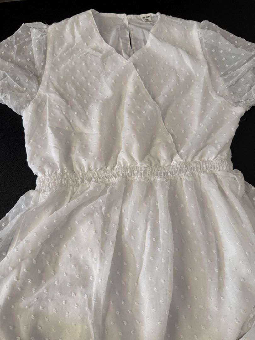 Shein White Dress (Category: Dresses) located in Bulacan. Submitted by emjay_17 (Listing ID 1436316670, Image 3). Description: White dress from Shein. Features a V-neckline and short, puffy sleeves. The dress has an elastic waist and a flowy skirt. The fabric has a subtle dotted texture. The dress is a size 16Y..