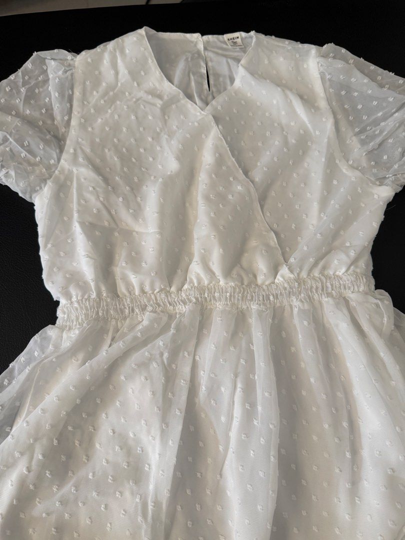 Shein White Dress (Category: Dresses) located in Bulacan. Submitted by emjay_17 (Listing ID 1436316670, Image 2). Description: White dress from Shein. Features a V-neckline and short, puffy sleeves. The dress has an elastic waist and a flowy skirt. The fabric has a subtle dotted texture. The dress is a size 16Y..