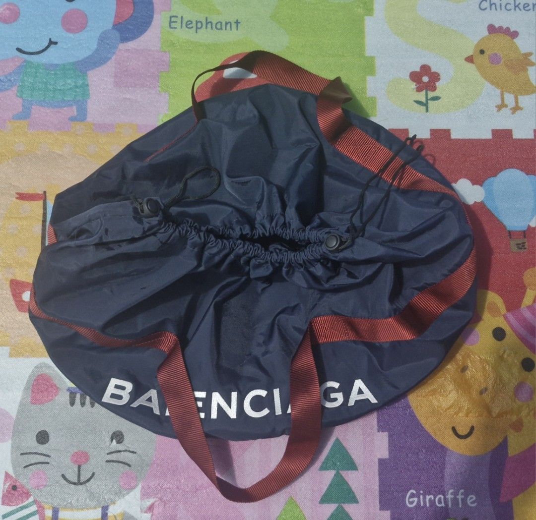 Balenciaga wheel duffle bag (Category: Luxury Bags & Wallets) located in Pili. Submitted by the_g_thrift (Listing ID 1436603192, Image 2). Description: - Balenciaga navy blue drawstring tote bag - Red strap and white Balenciaga logo - Drawstring closure - Circular base - Interior tag with brand name and "Paris" in gold - Serial number tag 19 diameter 14 length .