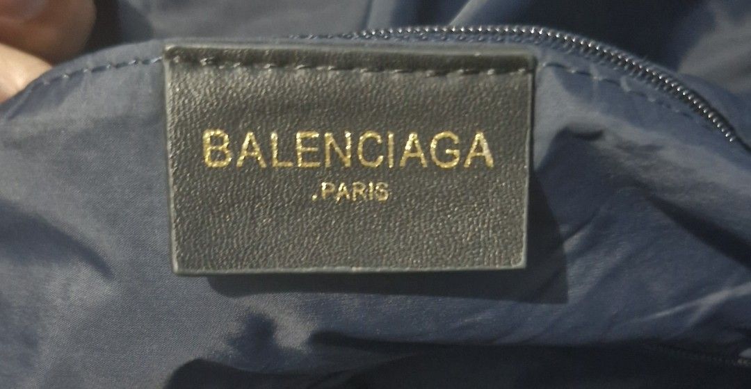 Balenciaga wheel duffle bag (Category: Luxury Bags & Wallets) located in Pili. Submitted by the_g_thrift (Listing ID 1436603192, Image 3). Description: - Balenciaga navy blue drawstring tote bag - Red strap and white Balenciaga logo - Drawstring closure - Circular base - Interior tag with brand name and "Paris" in gold - Serial number tag 19 diameter 14 length .