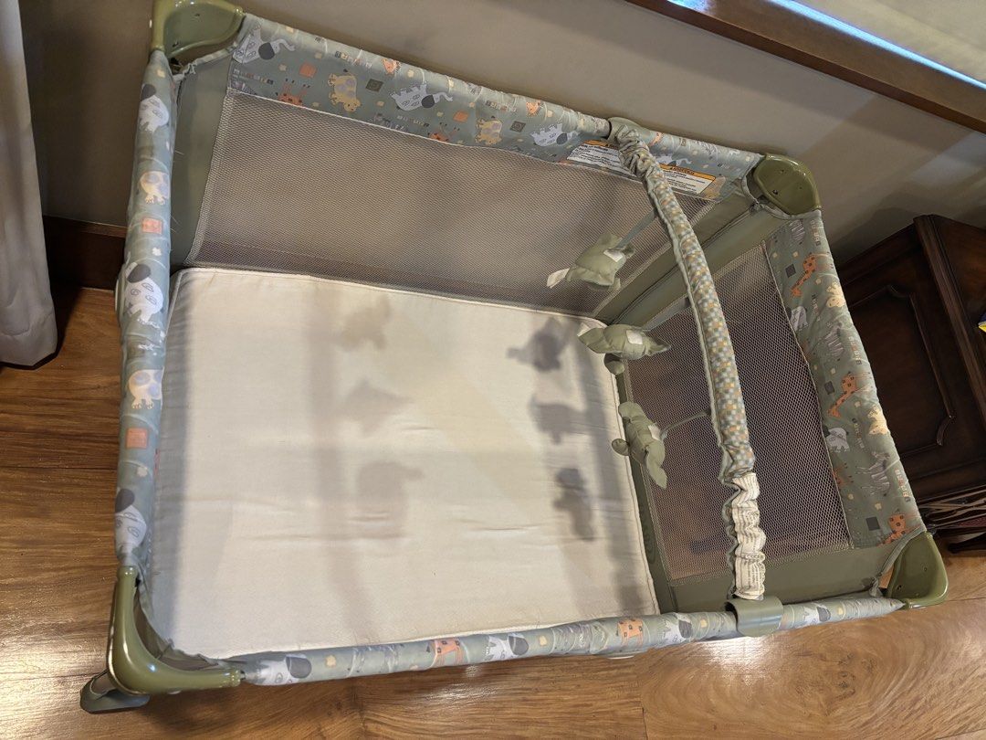 Graco Pack 'n Play Playard (Category: Cots & Cribs) located in Manila. Submitted by supersaleclub (Listing ID 1436650082, Image 2). Description: Graco Pack 'n Play playard features a playful animal print. It includes a mattress and a mobile with hanging toys. The playard has mesh sides for visibility and ventilation. There is a small hole in the mesh. The frame is a light green color..
