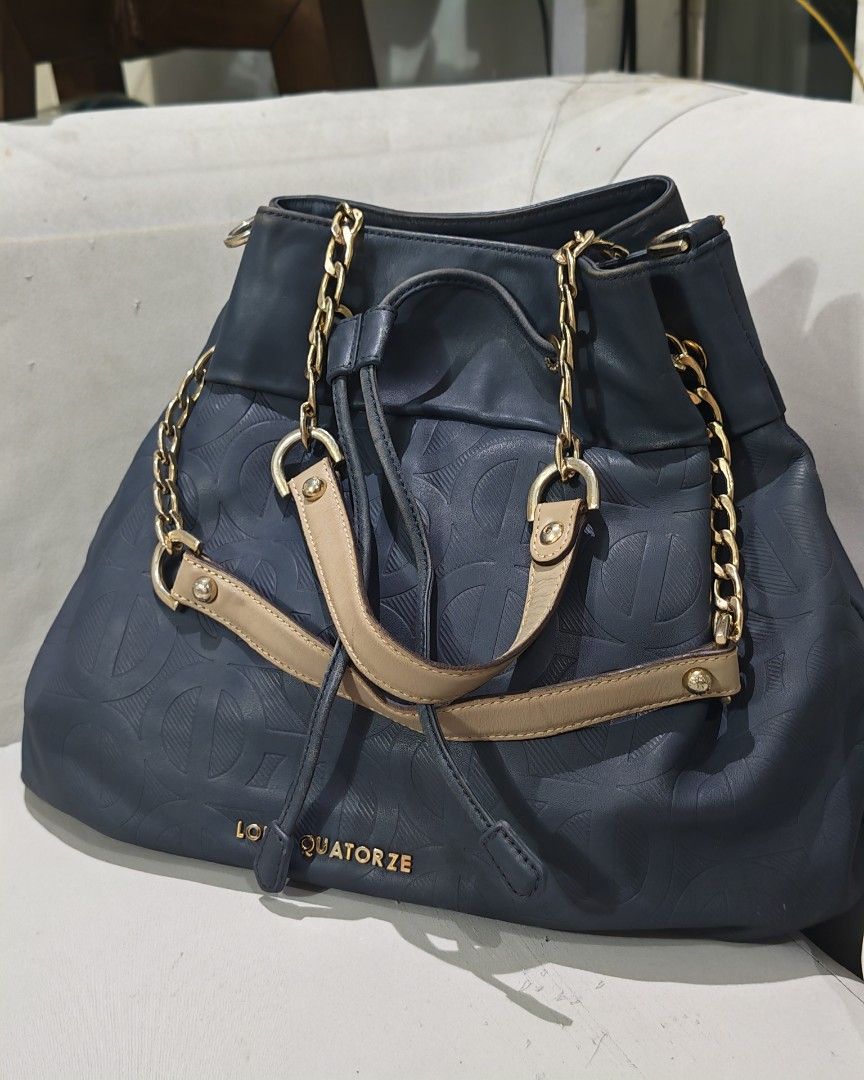 Louis Quatorze Handbag with Chain Straps (Category: Luxury Bags & Wallets) located in Paranaque City. Submitted by annyfd_1102 (Listing ID 1436581300, Image 1). Description: - Navy blue Louis Quatorze handbag - Elegant gold-tone chain straps - Secure drawstring closure - Convenient zippered back pocket - Stylish patterned interior lining - Features beige handle accents - Authentic Louis Quatorze branding.