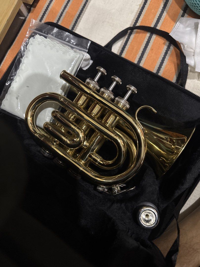 Mini Pocket Trumpet with Case (Category: Musical Instruments) located in Las Pinas. Submitted by yourchaiboy (Listing ID 1436542762, Image 1). Description: Budol buy. Just get it off my hands. - Mini pocket trumpet with gold finish - Includes case and cleaning cloth - Features three valves and a mouthpiece - Black case with handle for easy carrying - Compact and portable, ideal for travel.