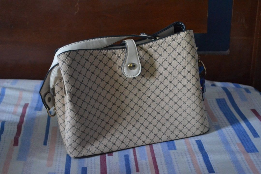 Beige Crossbody Handbag with Pattern (Category: Luxury Bags & Wallets) located in Valenzuela. Submitted by miss_merix (Listing ID 1436731686, Image 1). Description: - Beige handbag with a unique patterned design - White strap - Flap closure with gold-colored button - Multiple compartments, including a zippered one - Decorative charm included - Suitable for everyday use.