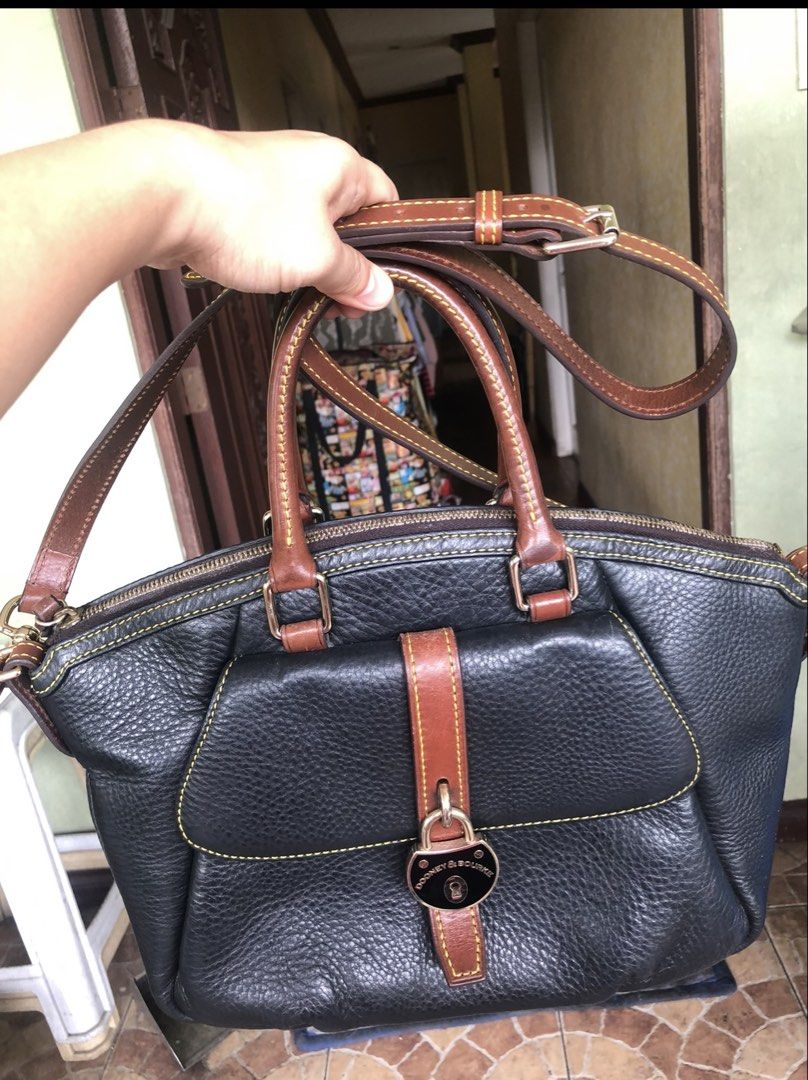 Dooney & Bourke Black Leather Handbag (Category: Luxury Bags & Wallets) located in Quezon City. Submitted by cprmob (Listing ID 1436752024, Image 1). Description: Black leather handbag with brown leather accents and stitching. Features a front flap with a buckle closure and a top zipper. Includes a detachable shoulder strap and double handles. The interior is red. The bottom of the bag has brown leather accents. The tag inside the bag has the num
