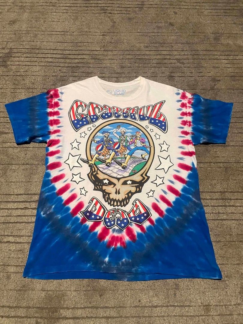 Grateful Dead Tie-Dye T-Shirt (Category: Tshirts & Polo Shirts ) located in Liloan. Submitted by r0yaxx (Listing ID 1436785781, Image 1). Description: - Vintage Grateful Dead tie-dye t-shirt - Dated 1993 - Features skull graphic with band members on the front - Eagle graphic with "Wave That Flag" on the back - Made by Liquid Blue - Red, white, and blue tie-dye pattern.
