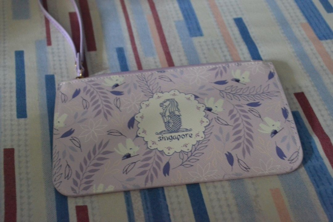 Singapore Souvenir Clutch (Category: Clutches) located in Valenzuela. Submitted by miss_merix (Listing ID 1436731384, Image 2). Description: - Light purple clutch - Floral pattern with Singapore design - Features the Merlion statue and the word "Singapore" - Includes a wrist strap - Zipper closure.