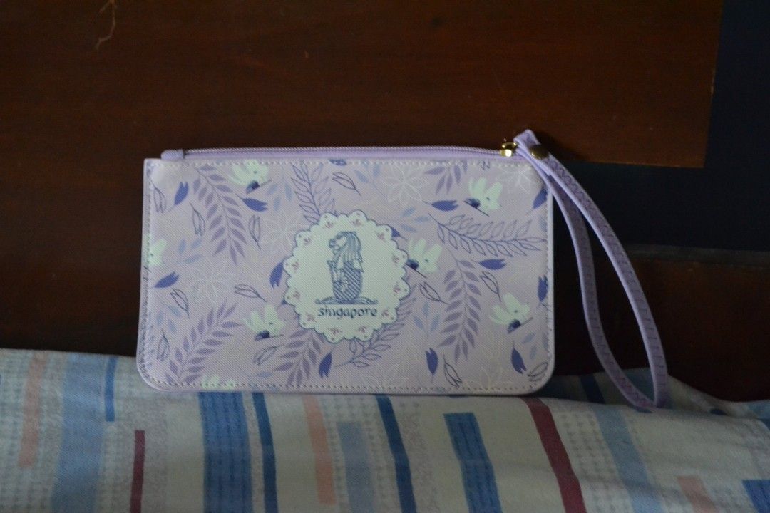 Singapore Souvenir Clutch (Category: Clutches) located in Valenzuela. Submitted by miss_merix (Listing ID 1436731384, Image 1). Description: - Light purple clutch - Floral pattern with Singapore design - Features the Merlion statue and the word "Singapore" - Includes a wrist strap - Zipper closure.