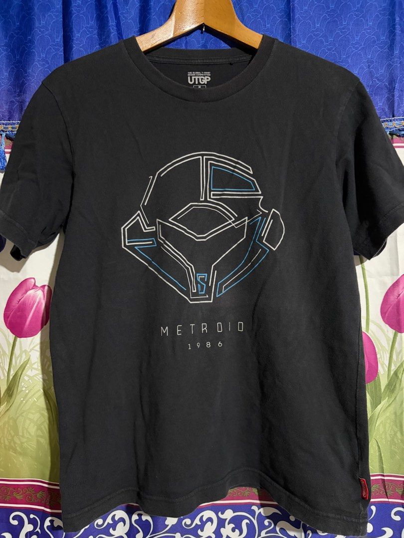 UTGP Nintendo Metroid T-shirt (Category: Tshirts & Polo Shirts ) located in Santa Barbara. Submitted by pickersdelight (Listing ID 1436789384, Image 1). Description: - Black UTGP T-shirt - Features a Metroid design - Graphic: Samus Aran's helmet - Text: "METROID 1986" - Includes Nintendo tag - Size: M Dimension: Width: 21 inches Length: 26 inches Note: colors may vary due to lighting .