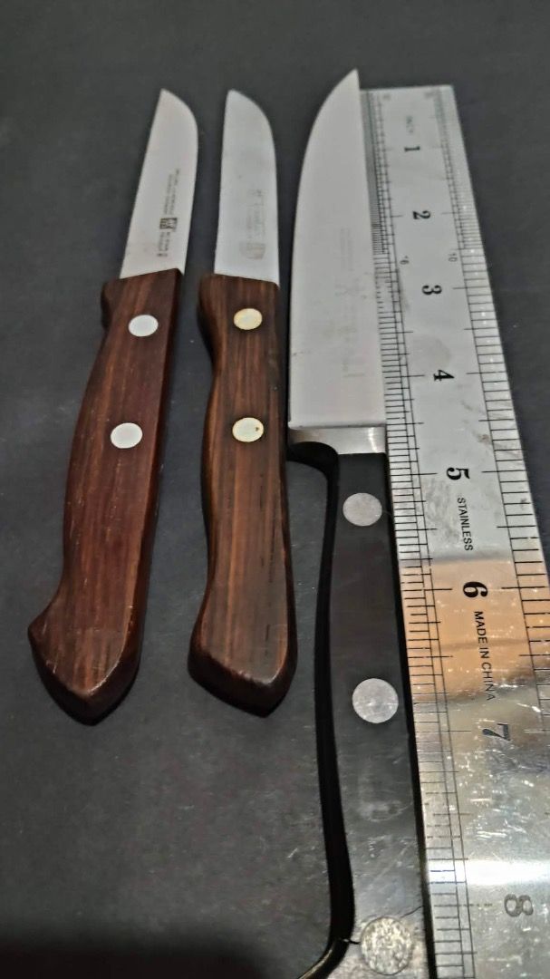 Zwilling J.A. Henckels Knife Set (Category: Knives & Chopping Boards) located in Manila. Submitted by ganisurplus21 (Listing ID 1436675179, Image 3). Description: - Set of three Zwilling J.A. Henckels knives. - Includes: - One large knife with a black handle. - Two smaller knives with wooden handles. - Features the Zwilling J.A. Henckels logo on the blades. - Perfect for various kitchen tasks..