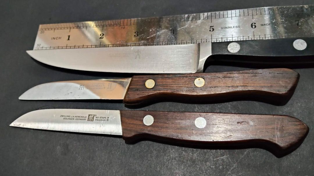 Zwilling J.A. Henckels Knife Set (Category: Knives & Chopping Boards) located in Manila. Submitted by ganisurplus21 (Listing ID 1436675179, Image 2). Description: - Set of three Zwilling J.A. Henckels knives. - Includes: - One large knife with a black handle. - Two smaller knives with wooden handles. - Features the Zwilling J.A. Henckels logo on the blades. - Perfect for various kitchen tasks..